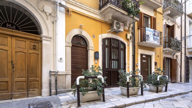 Una calle con un edificio amarillo, puertas de madera y plantas en macetas.