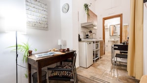 Cocina compacta con fregadero, estufa y armarios, comedor con mesa y sillas, y un pequeño espacio de trabajo con escritorio y silla.