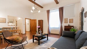 Een woonkamer met een bank, een fauteuil, een salontafel en een eethoek met stoelen en een tafel.