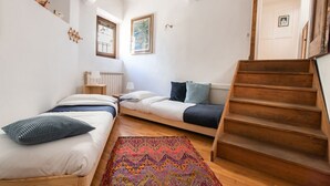 Een slaapkamer met twee bedden, een kleurrijk tapijt, houten trap en een raam.