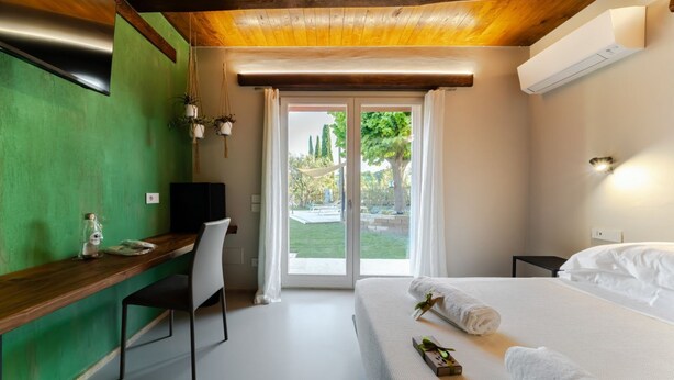 Une pièce comprenant un lit, un bureau, une chaise, un téléviseur et une porte-fenêtre coulissante donnant sur l’extérieur.