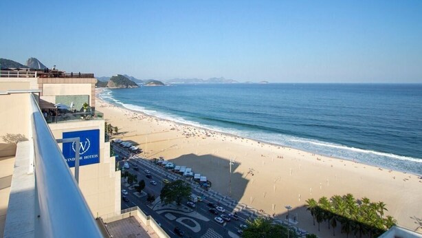 Blick auf den Strand vom Hotelbalkon, mit blauem Himmel, Sandstrand und ruhiger See.