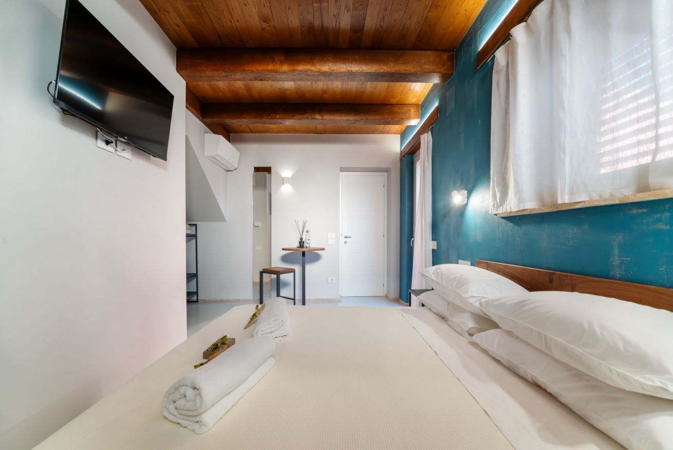 Une chambre à coucher avec un lit, un téléviseur fixé au mur, une petite table avec une plante et une fenêtre avec des rideaux.