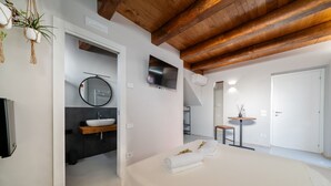 A modern bedroom with a large bed, a TV, a mirror, and a small table with a vase.