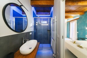 Ein modernes Badezimmer mit rundem Spiegel, weißem Waschbecken, einer Duschkabine aus Glas und Holzboden.