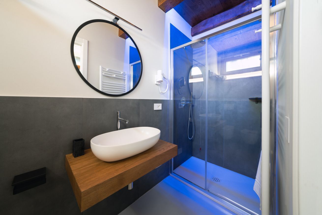 Een moderne badkamer met een groot ovaal wastafel, een ronde spiegel en een douche met glazen wanden.