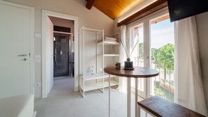 Una habitación moderna con techo de madera, un balcón con vistas, una puerta blanca y una pequeña mesa con un florero.