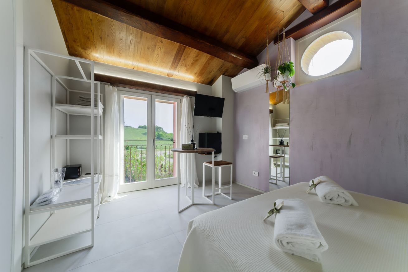 Ein Schlafzimmer mit Bett, Fernseher, einem Balkon mit Aussicht und einer Holzbalkendecke.