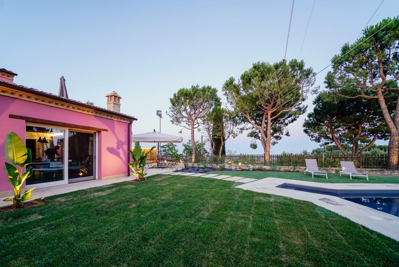 Un jardin avec une piscine, une maison rose et une pergola.