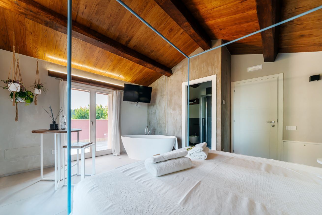 Une chambre avec un grand lit, une baignoire, une télévision et un balcon agrémenté de plantes.