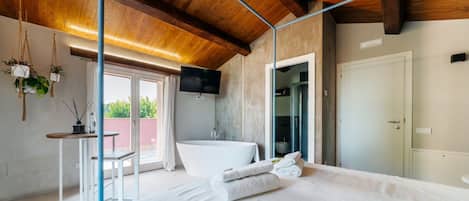 A bedroom with a large bed, a bathtub, a TV, and a balcony with plants.