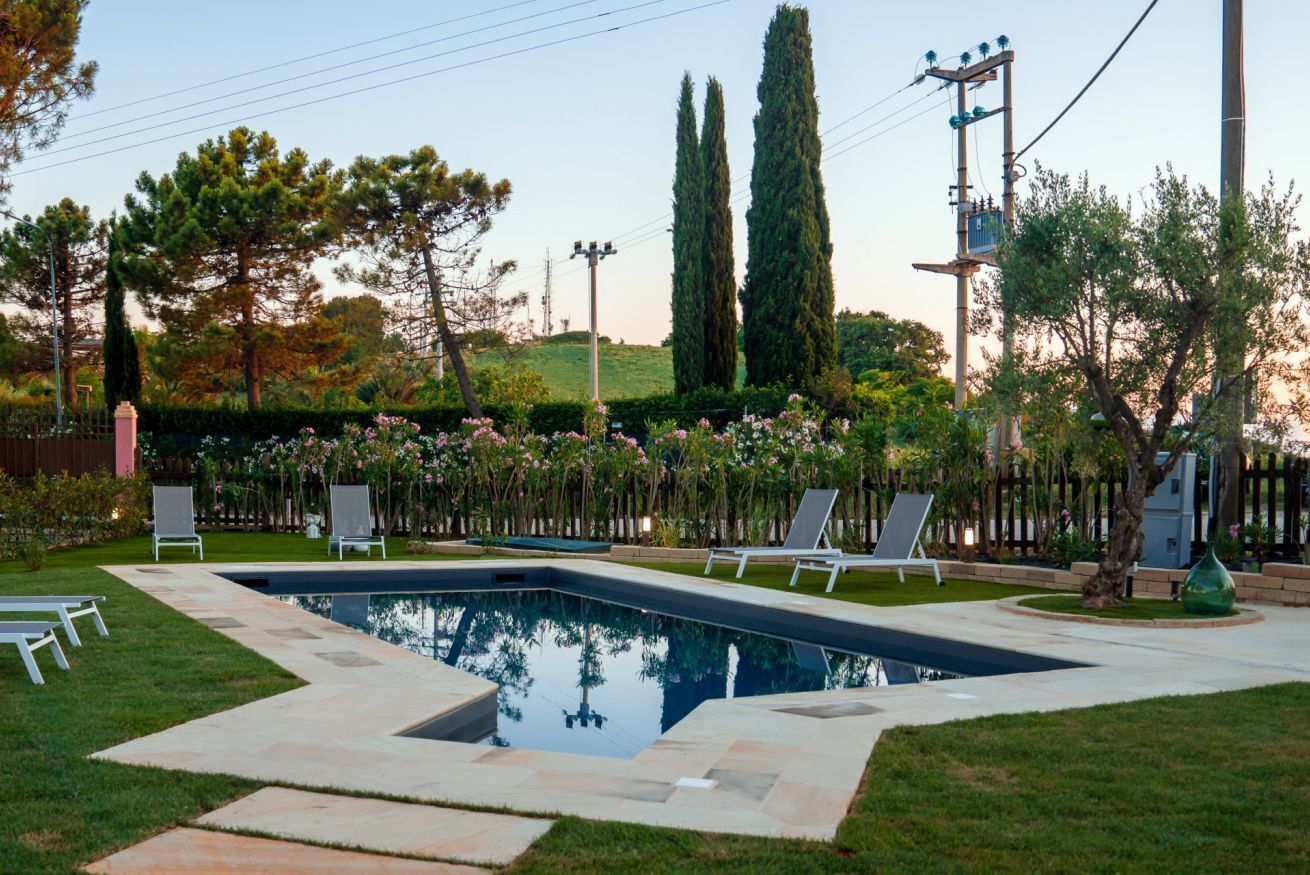 Une piscine entourée de chaises longues, une pelouse et de grands arbres en arrière-plan.