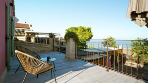 A balcony with a view of the sea, wicker chairs, a small table, and a stone pillar. -  L’Organetto Luxury B&B - Aurora Suite (Alberelli)
