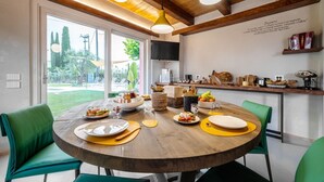A dining area with a round wooden table, green chairs, and a kitchen in the background. -  L’Organetto Luxury B&B - Aurora Suite (Alberelli)