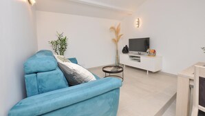 Una sala de estar moderna con un sofá azul, un mueble blanco para entretenimiento y un televisor.