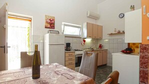 Eine kompakte Küche mit Kühlschrank, Herd und Spüle. Esstisch mit einer Flasche und Gläsern.