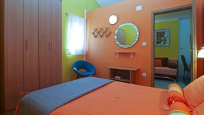 Ein Schlafzimmer mit Bett, Sessel, Kleiderschrank, Spiegel und einem kleinen Tisch.