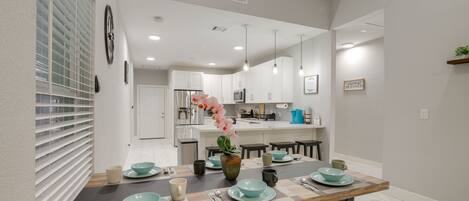 A modern kitchen with white cabinets, a central island, and a dining area with a wooden table set for four.