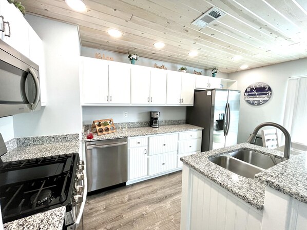 Una cocina moderna con armarios blancos, encimeras de granito, electrodomésticos de acero inoxidable y un reloj en la pared.