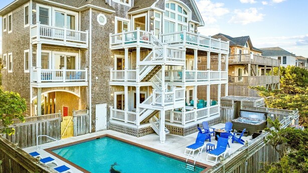 Una casa de varios pisos con piscina, balcones y una terraza de madera.