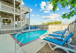 A swimming pool with blue lounge chairs, a wooden deck, and a white staircase.