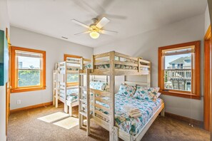 A room with bunk beds, a ceiling fan, and large windows.