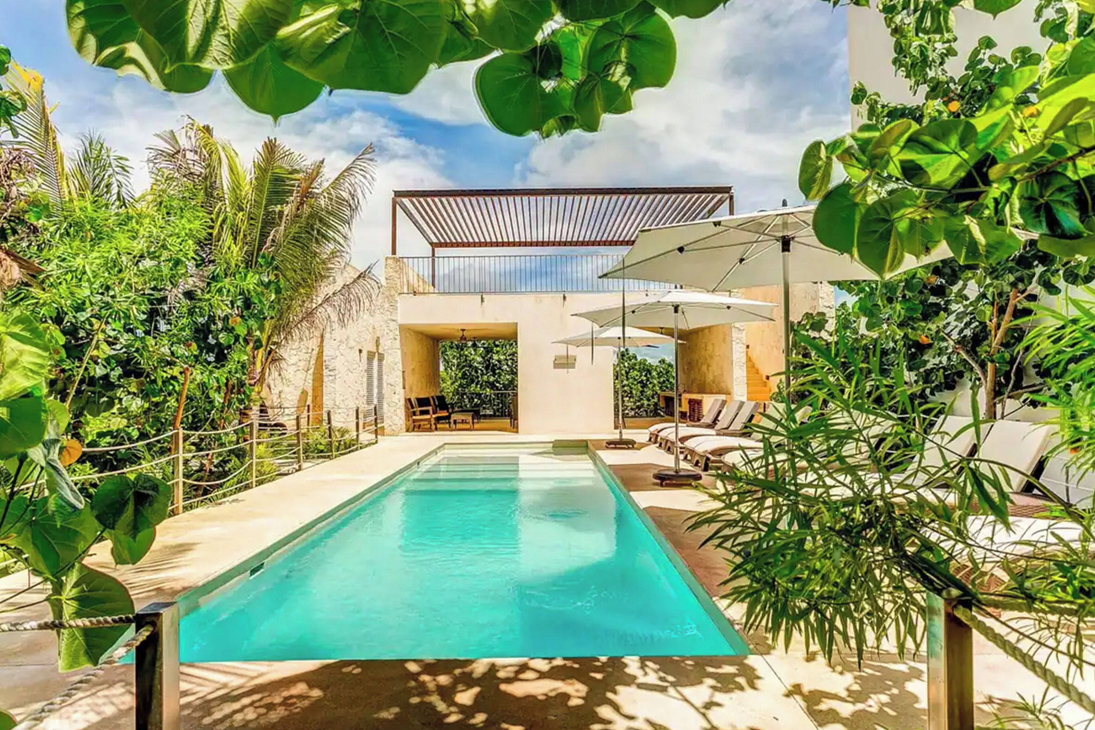 Un área de piscina moderna con una piscina cristalina, sillones de descanso y sombrillas.