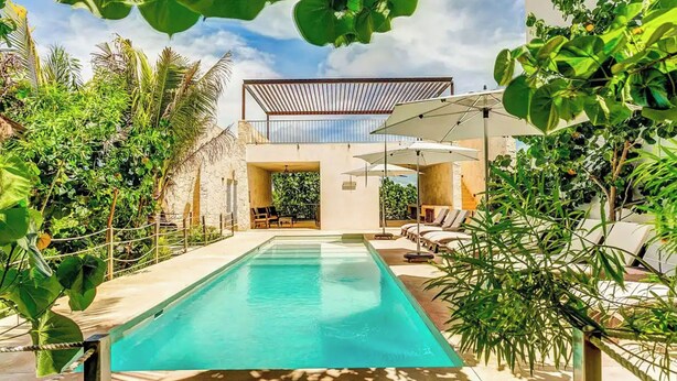 A modern pool area with a clear pool, lounge chairs, and umbrellas.