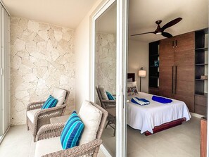 A room with wicker furniture, a bed with a white bedspread, a ceiling fan, and a stone wall.
