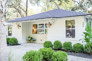 A white house with a dark roof, numbered 409, featuring a front porch with potted plants and two wall-mounted lanterns.