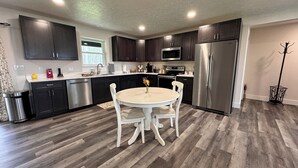 A modern kitchen with dark cabinets, stainless steel appliances, and a white dining table with chairs. - Close to everything-tucked away from the noise. A brand-new, blissful stay. (Ithaca)