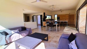 A modern living room with a sofa and a coffee table, a dining area with a table and chairs, and a kitchen in the background. - Villa Florida, Pinarello, 8 pers, piscine chauffée, 350 m plage à pieds (STE LUCIE DE PORTO VECCHIO)