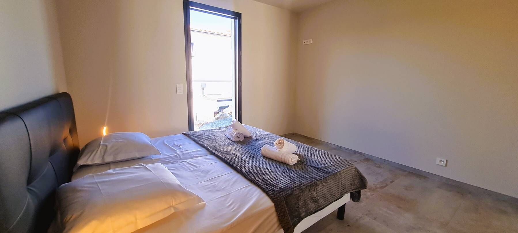 A single bed with white linens and a dark headboard, a small window, and a plain wall.