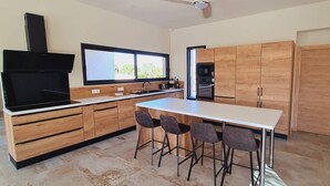 A modern kitchen with wooden cabinets, a large island with bar stools, a built-in oven, and a black range hood. - Villa Florida, Pinarello, 8 pers, piscine chauffée, 350 m plage à pieds (STE LUCIE DE PORTO VECCHIO)
