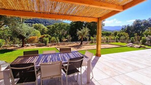 An outdoor patio with a wooden pergola, a table with chairs, and a view of a landscaped garden with trees and a pool. - Villa Florida, Pinarello, 8 pers, piscine chauffée, 350 m plage à pieds (STE LUCIE DE PORTO VECCHIO)