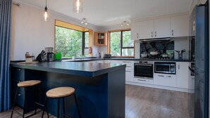 A modern kitchen with a central island, bar stools, built-in appliances, and large windows. - Comfort, Style, Relaxation. Your Home Away from Home Awaits! (Blenheim)