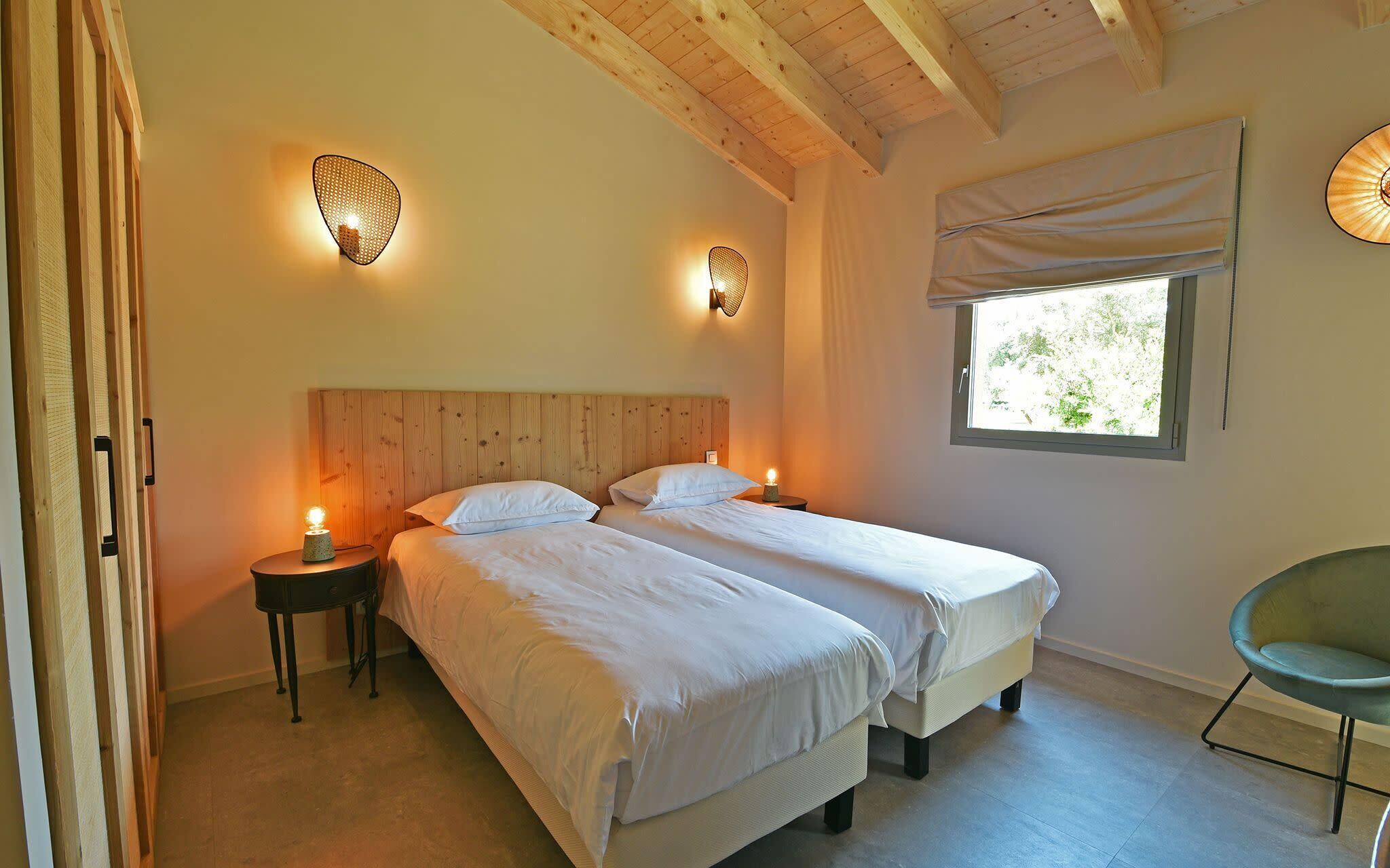 Une chambre avec deux lits, une tête de lit en bois, des lampes de chevet, une fenêtre avec des rideaux et une chaise.