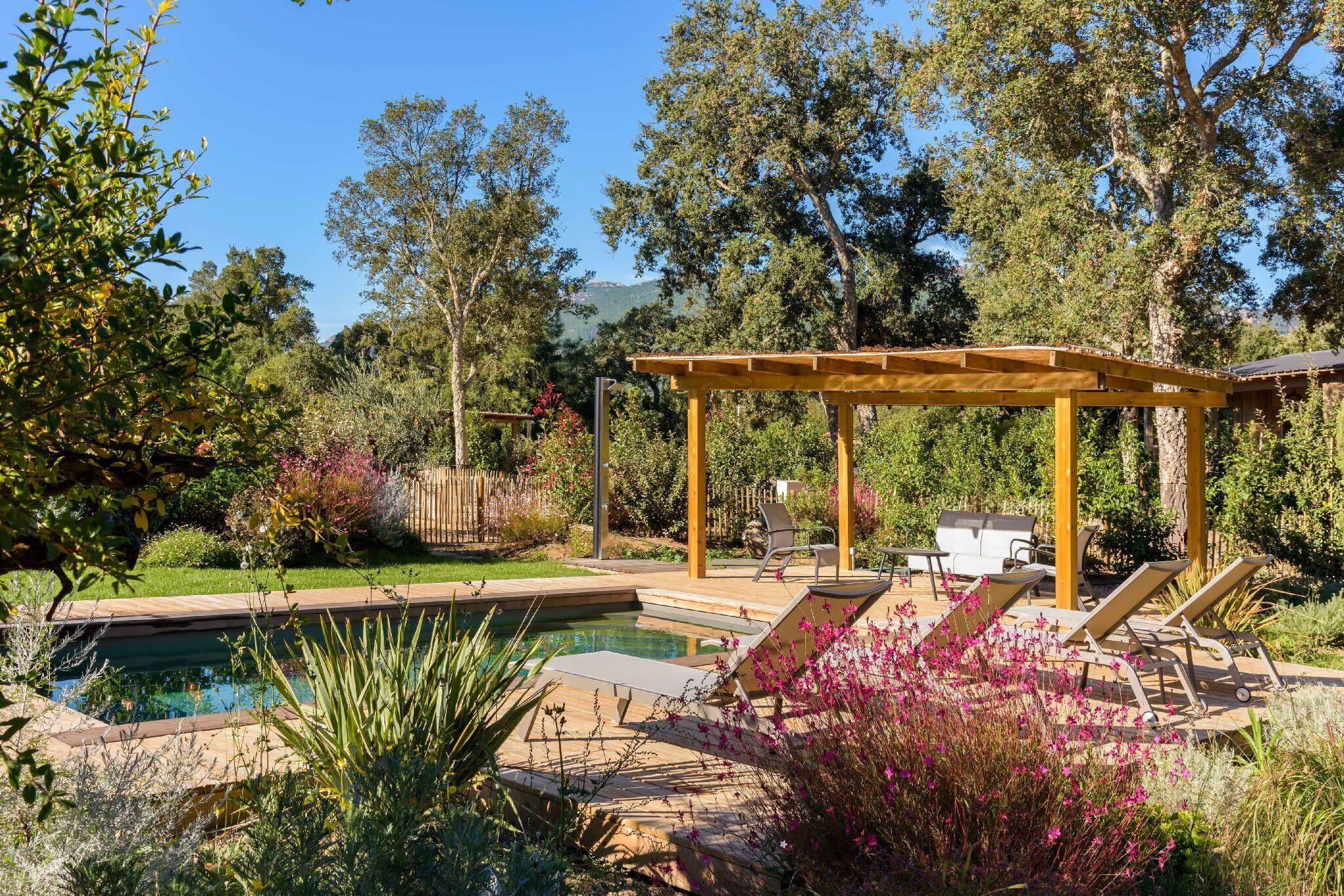 A pool area with a pergola, lounge chairs, and a small table.