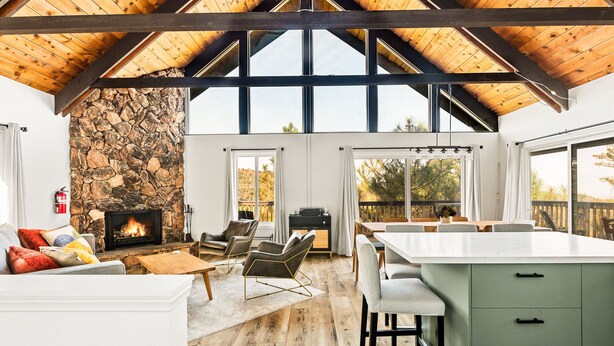 A spacious living area with a stone fireplace, wooden ceiling beams, and large windows. - EV Charger, Dogs welcome at Sunset Ridge! (Lake Arrowhead)