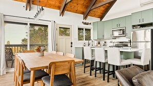 A spacious kitchen with wooden beams, a dining area with a table and chairs, and a view of the outdoors. - EV Charger, Dogs welcome at Sunset Ridge! (Lake Arrowhead)