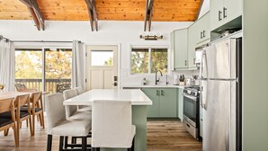 A modern kitchen with a wooden ceiling, a dining area with a table and chairs, and a view of trees outside. - EV Charger, Dogs welcome at Sunset Ridge! (Lake Arrowhead)