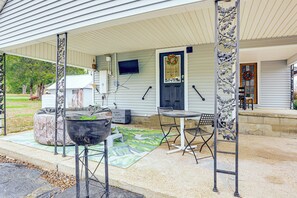 A covered porch with a grill, outdoor seating, and a television mounted on the wall.