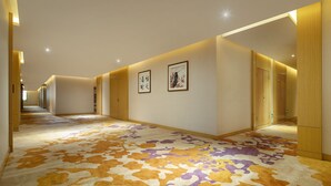 Un pasillo de hotel con puertas de madera, obras de arte enmarcadas en las paredes y alfombra estampada.