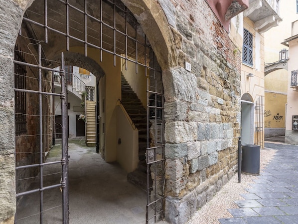 A stone building with a metal gate, a staircase, and a narrow alleyway.