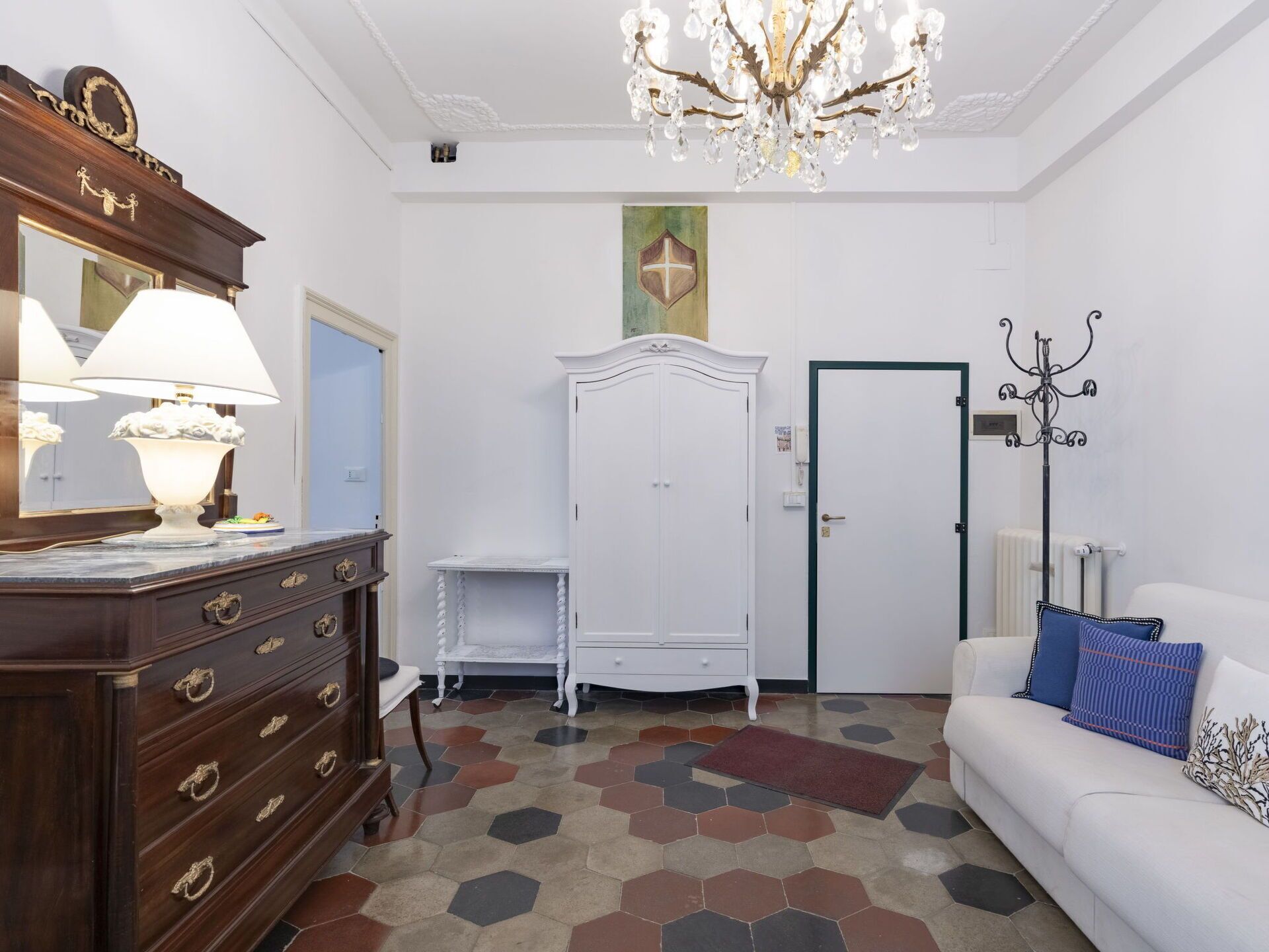 Een kamer met een houten dressoir, een witte garderobe, een witte bank met blauwe kussens, een kroonluchter en een vloer met een honingraatpatroon.