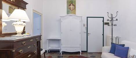 Een kamer met een houten dressoir, een witte garderobe, een witte bank met blauwe kussens, een kroonluchter en een vloer met een honingraatpatroon.