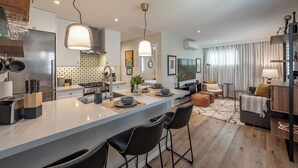 A modern kitchen with a large island, bar stools, and a dining area with a sofa and a TV. - 1-Bd 1-Bth Apt, Disney & Anaheim Conv Ctr in 10 Mins! Full Kitchen & Outdr Space (Santa Ana)