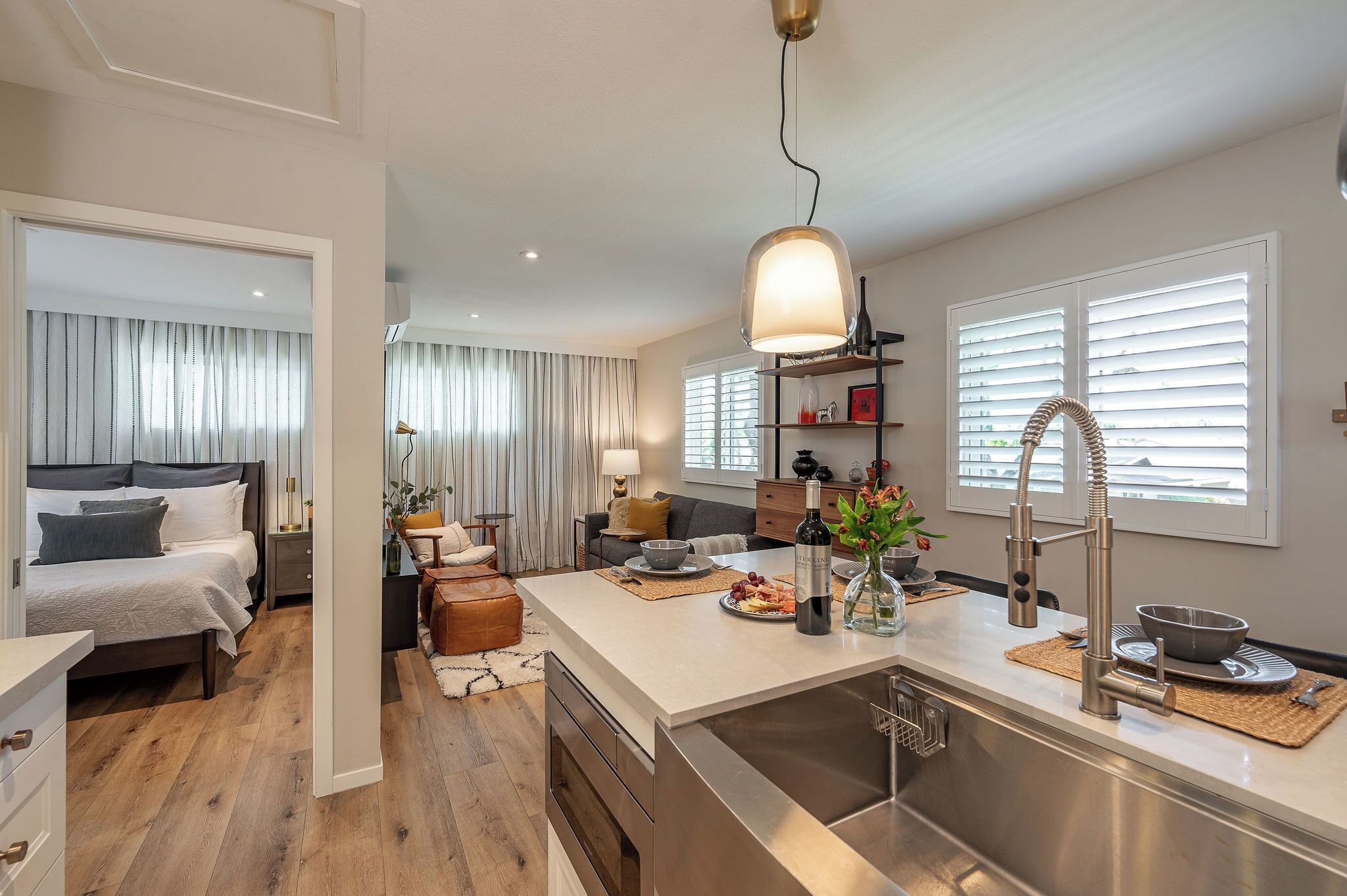 A modern hotel room with a large bed, a separate sitting area, a kitchenette, and a bathroom.
