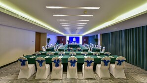 Un salón de conferencias con una larga mesa, sillas blancas con cintas azules y un fondo azul con el texto "MEADOW LESTER".