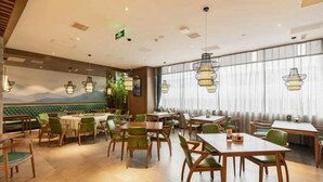 Un restaurante con mesas redondas y sillas verdes, un mural de montañas y lámparas colgantes.